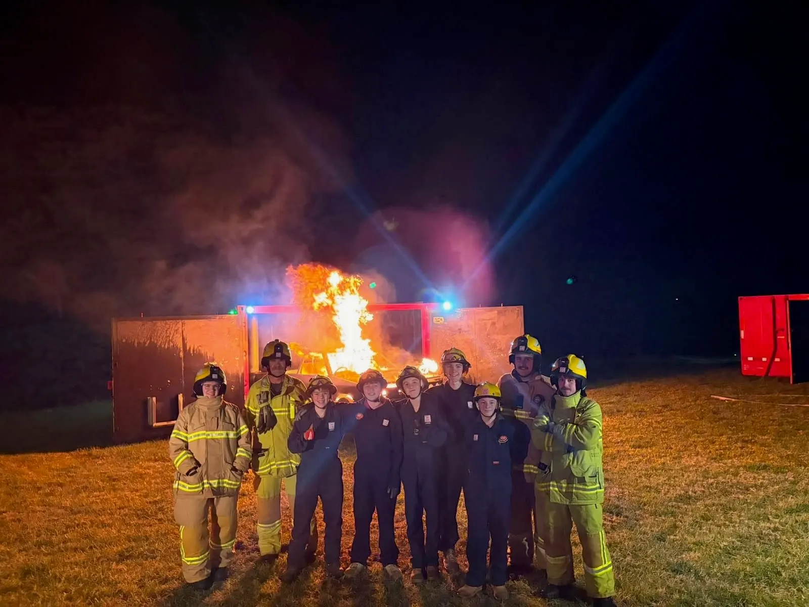 Red Hill CFA juniors and leaders in protective clothing in front of a controlled training fire at night